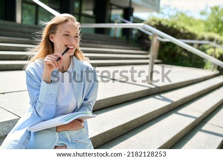 Pretty smiling girl university student holding notebooks looking away sitting on stairs inspired for writing outdoors. College study programs, academic educational courses, learning classes concept. Royalty-Free Stock Photo #2182128253