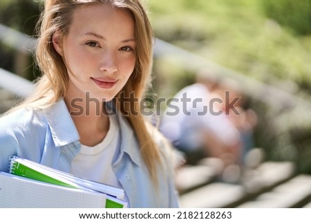 Smiling smart pretty happy blonde girl university or college student holding notebooks looking at camera standing outside campus. Close up portrait outdoors, education program course ads.