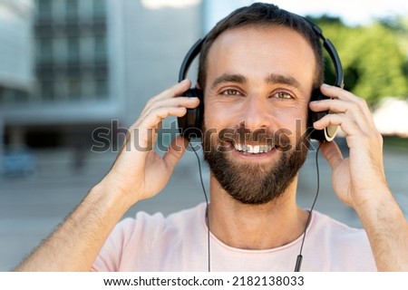 Close up portrait of confident smiling latin man listening music in stylish headphones looking at camera outdoors 