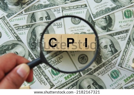 CPI, consumer price index symbol. hand holding magnifying glass investigating wooden block with words CPI, consumer price index on dollar bills. Business and CPI, consumer price index concept. Royalty-Free Stock Photo #2182167321