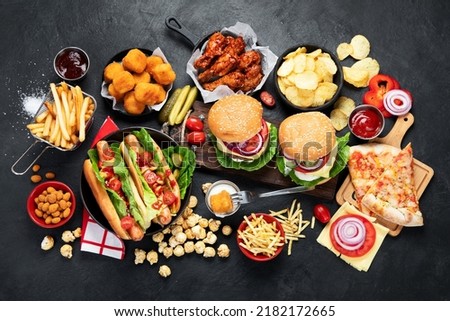 Fast food and unhealthy eating concept - close up of fast food snacks and cola drink on a dark background, top view. Royalty-Free Stock Photo #2182172665