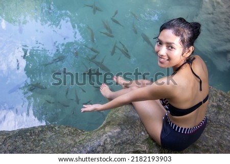 A young woman in swimsuit showing fish in clear water