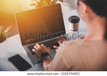Web application development. programmer woman writing program code sitting at workplace in office, software developer hands coding HTML programming with laptop computer, IT start up concept, back view