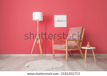 Comfortable armchair with table and lamp near pink wall in room
