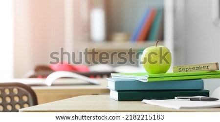 Apple and school stationery on desk in classroom