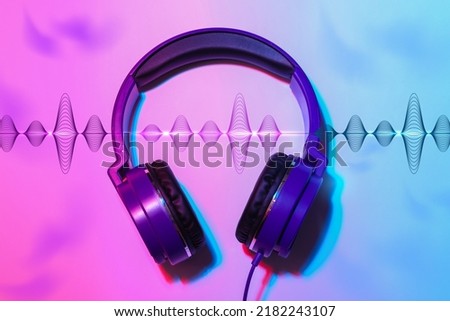 Modern headphones with illustration of dynamic sound waves on color background, top view