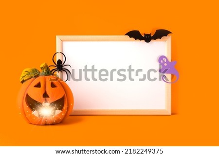 Halloween holiday concept. Jack o lantern, light, handmade paper decorations, spider, ghost, bat and blank frame on orange background. Halloween festival party, greeting card with mockup copy space.
