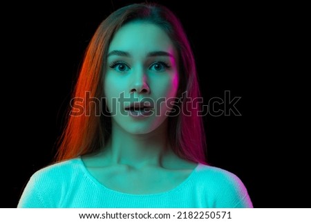 Portrait of young emotive girl posing, showing shocked expression isolated over black studio background in neon light. Concept of beauty, fashion, emotions, facial expression, youth, lifestyle, ad