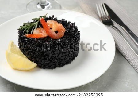 Delicious black risotto with shrimps and lemon on marble table, closeup