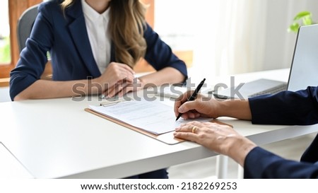 A male client sign his signature in a agreement contract paper in front of his female realtor in the office. cropped image