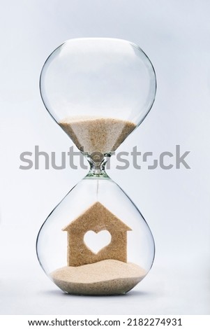 Time is a shelter. Building a home with love concept with falling sand taking the shape of a heart house inside a hourglass. Royalty-Free Stock Photo #2182274931