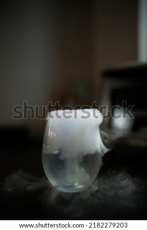 Closeup glass with white fog at dark background. Chemical reaction of dry ice with water.