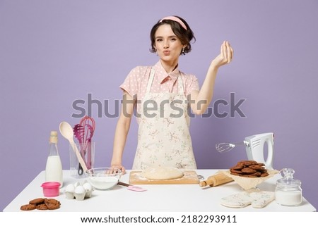Young fun housewife housekeeper chef cook baker woman in pink apron work at table kitchenware make okay taste delight sign delicious isolated on pastel violet background. Process cooking food concept.