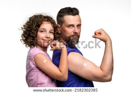Family in basic t-shirts showing biceps with band-aid after vaccine injection. Dad and daughter 10-12s wear pink and violet t-shirts on white studio wall. Antiviral immunization. Revaccination Royalty-Free Stock Photo #2182302385