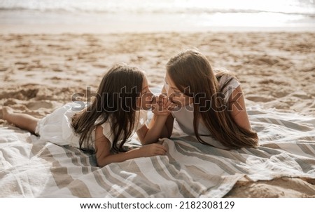 Loving mom and daughter holding and kissing hands while lying on blanket on summer weekend day on sandy beach