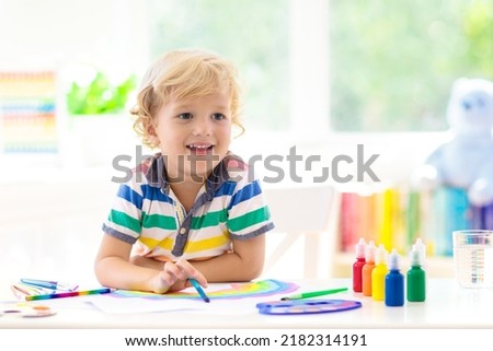 Kids paint. Child painting in white sunny study room. Little boy drawing rainbow. School kid doing art homework. Arts and crafts for kids. Paint on children hands. Creative little artist at work.