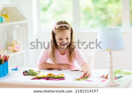 Child creating picture with colorful leaves. Art and crafts for kids. Little girl making collage image with rainbow plant leaf. Biology homework for young school student. Creative autumn home fun.