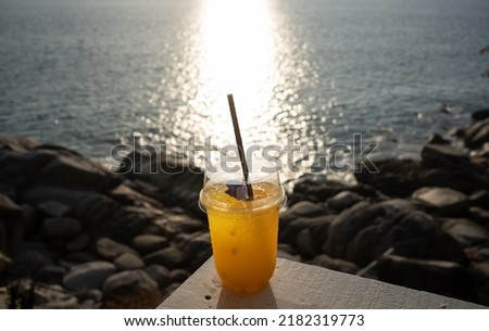 Cup orange juice on top table seaside during sunset sky daylight. Close-up Fresh orange cocktail in glass cafe holiday coconut trees background. Water drink summer copy space 2022. no people