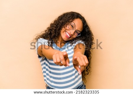 Young hispanic woman isolated on beige background pointing to front with fingers.