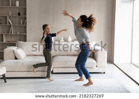 Excited active mom and happy daughter kid having fun, going wild, dancing to music in living room, jumping on floor, practicing exercises, moving bodies, listening to radio. Home activity concept