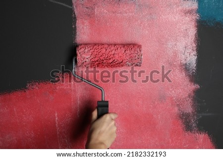Woman painting grey wall with pink dye, closeup