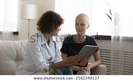 Confident doctor and woman patient discuss test results on pad screen on appointment at oncological center. Qualified physician explain treatment plan to young female sick with cancer using tablet pc Royalty-Free Stock Photo #2182348137