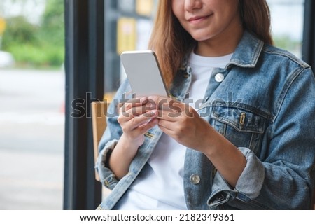Closeup image of a young woman holding and using mobile phone
