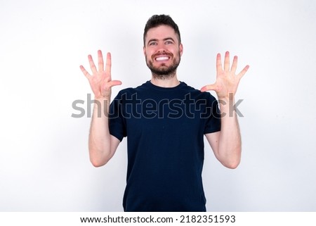 Young caucasian man wearing black T-shirt over white background showing and pointing up with fingers number ten while smiling confident and happy.