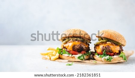 Two craft cheeseburgers and fries on parchment paper over grey concrete background. Copy space. Web banner burgers Royalty-Free Stock Photo #2182361851