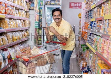 Happy man showing blank screen of mobile phone at grocery store Royalty-Free Stock Photo #2182376005