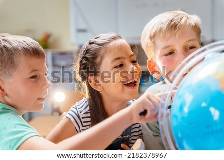 Joyful enthusiastic children pupils find something at the globe at classroom at school. Geography worldwide explorer continent country concept. Royalty-Free Stock Photo #2182378967