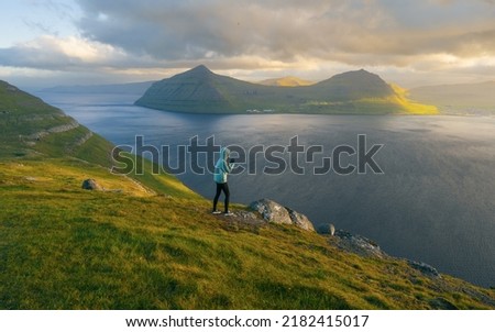 Lonely tourist in blue jacket looking over majestic fjords on Faroe Islands. Landscape photography. Great sunset view from populat tourist attraction - Klakkur peak