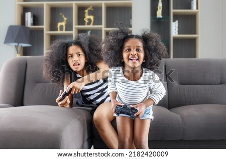 Black sister and cute African American woman having fun holding game joystick sitting on the sofa relaxing together at the home concept of childhood copy space mockup Play games with a joystick.