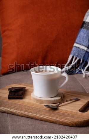 Autumn mood composition with cup of cocoa and chocolate, plaid and books on sofa background. Hot drink in autumn concept.