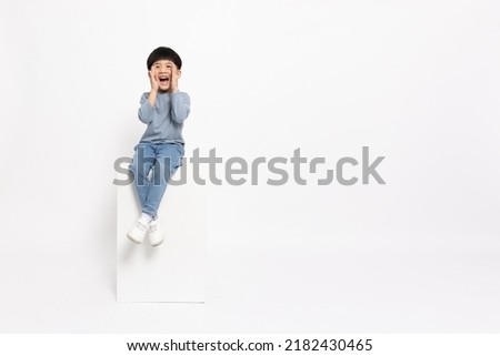 Asian little boy sitting on white box and open mouths raising hands screaming announcement isolated on white background, Full body composition and five years old Royalty-Free Stock Photo #2182430465