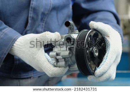 A power steering pump is in the hands of an auto mechanic. Close-up. Compliance and integrity control of the new spare part. Repair and maintenance of a car in a car service center. Royalty-Free Stock Photo #2182431731