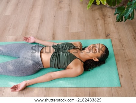 A young multi-ethnic woman lies in Shavasana yoga pose at the end of practice Royalty-Free Stock Photo #2182433625