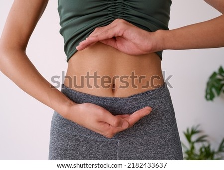 Close up of a young multi-ethnic woman's stomach cupped by her hands Royalty-Free Stock Photo #2182433637