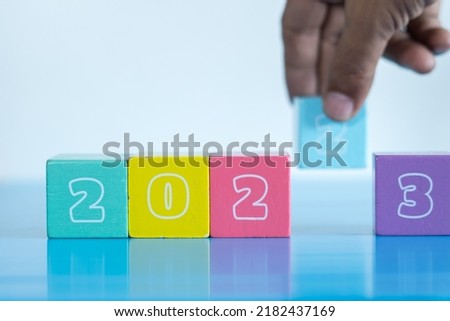 Selective focus shot of a conceptual of new year. Year 2022 ending and 2023 incoming idea. Hand taking out 2 representing end of the year and 3 the sign of new year. 