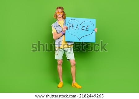 Full length body size view of attractive cheerful guy holding paper peace sign isolated over bright green color background