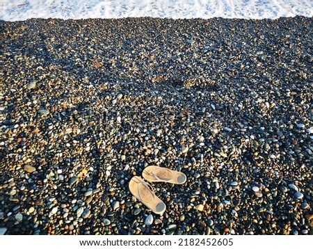 Pair of flip flops on pebble beach in front of the sea on summer vacation. Beautiful sunshine and shadows. travel Concept image. copy space