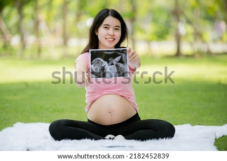 An Asian woman who is pregnant for the first time sits and relaxes to show her images from a hospital ultrasound to check the health of her growing baby