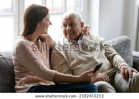 Laughing millennial granddaughter willing explain teach interested aged grandfather to use mobile phone apps. Caring young daughter hug warm beloved retired dad order buy goods for him online by cell Royalty-Free Stock Photo #2182453213