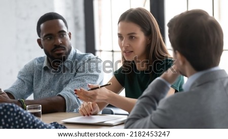 Millennial team of interns or employees brainstorming at business training set, discussing project tasks. Young female manager speaking and sharing ideas with colleagues, reviewing sales report Royalty-Free Stock Photo #2182453247