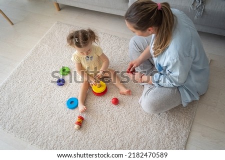 Mother and daughter are playing games in the excitement of the house. High angle view of the cute woman and kid girl playing educational wooden eco friendly toys at home  Royalty-Free Stock Photo #2182470589