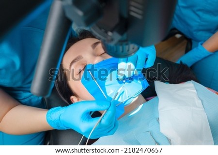 Photo endodontic treatment of dental canals in the lower molar permanent tooth molar with endodontic file with apex locator, tooth with clamp attached to it by cofferdam Royalty-Free Stock Photo #2182470657