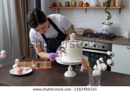 Woman in an apron decorates cake with chocolate figures for holiday. There are tools on table. Selective focus. Photos about confectioners, food, hobbies.