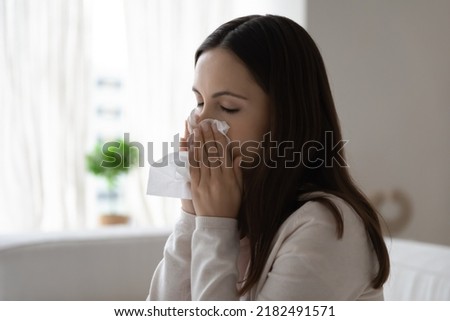 I have caught cold. Sad ill young woman sitting on bed sofa couch with closed eyes feeling bad broken hiding running nose in handkerchief suffering of flu respiratory viral infection seasonal allergy Royalty-Free Stock Photo #2182491571