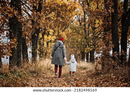 Mother and little baby daughter walking together in autumn park, forest. Mother with toddler daughter