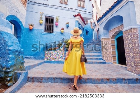 Colorful traveling by Morocco. Young woman in yellow dress walking in  medina of  blue city Chefchaouen. Royalty-Free Stock Photo #2182503333